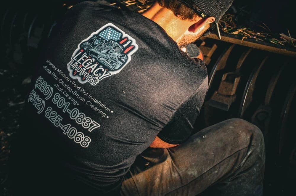 Worker repairing equipment wearing Legacy Handworks shirt with contact information.