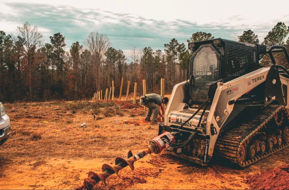 Terex DT170 compact track loader drilling holes for fence posts in a wooded area.