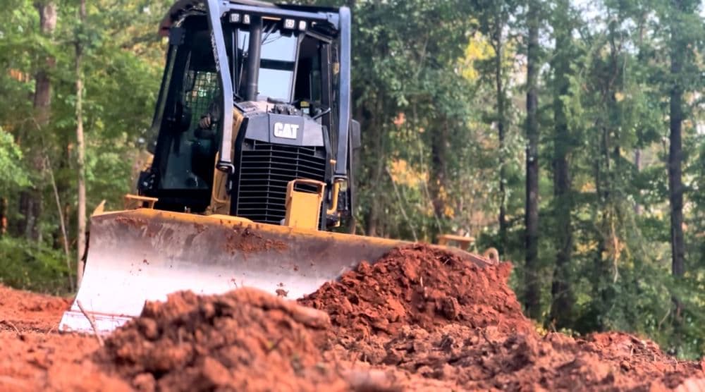 CAT bulldozer on a construction site pushing dirt in a forested area.