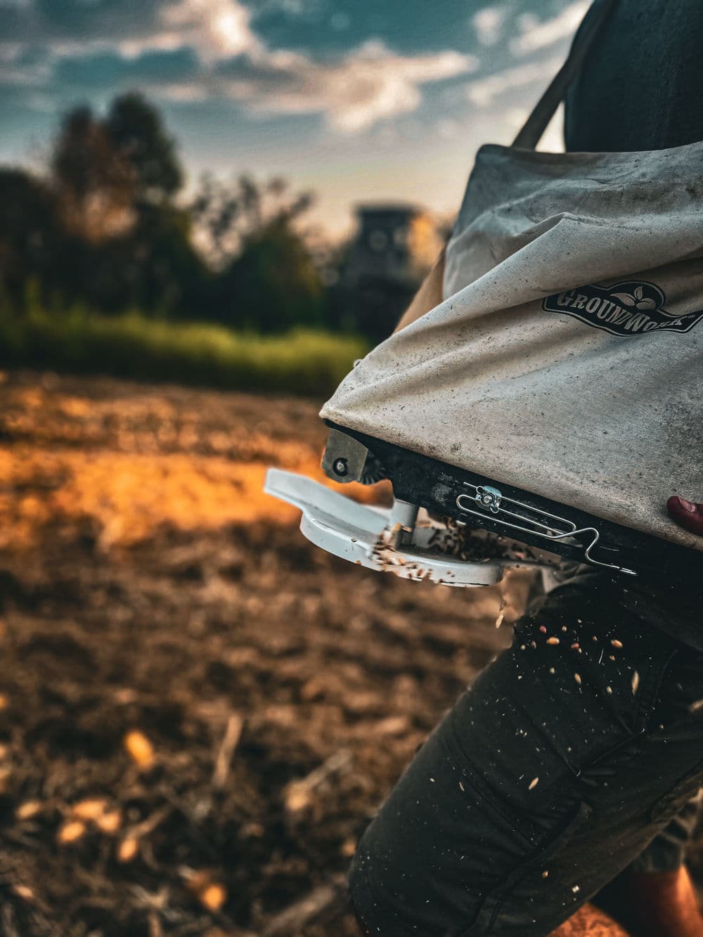 Person using a seed planter in a field, with soil and seeds spilling from the machine.
