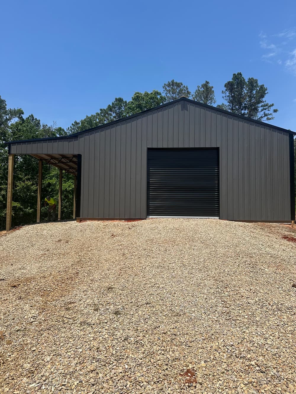 Modern gray metal garage building on gravel driveway surrounded by trees.